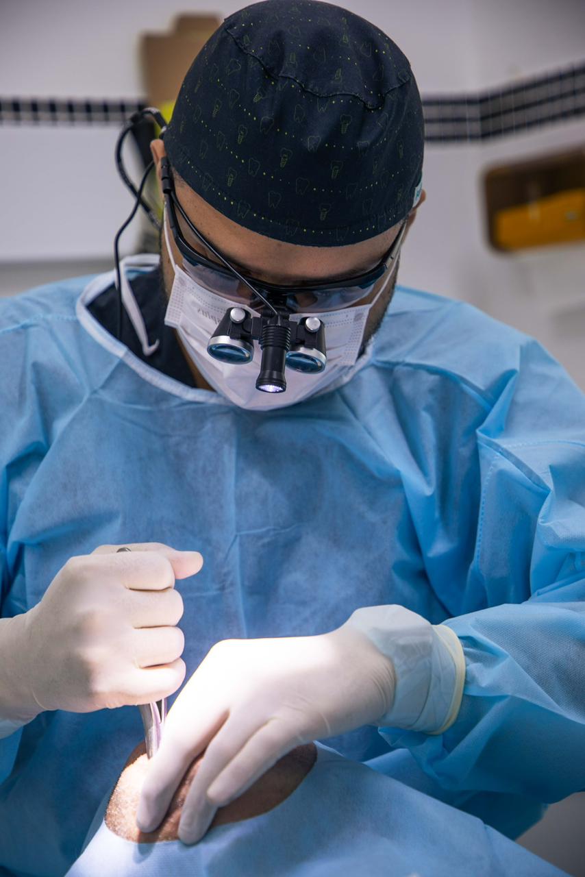 Dr. Renato Apolinário em cirurgia de implante, com lupa de magnificação e iluminação focal.