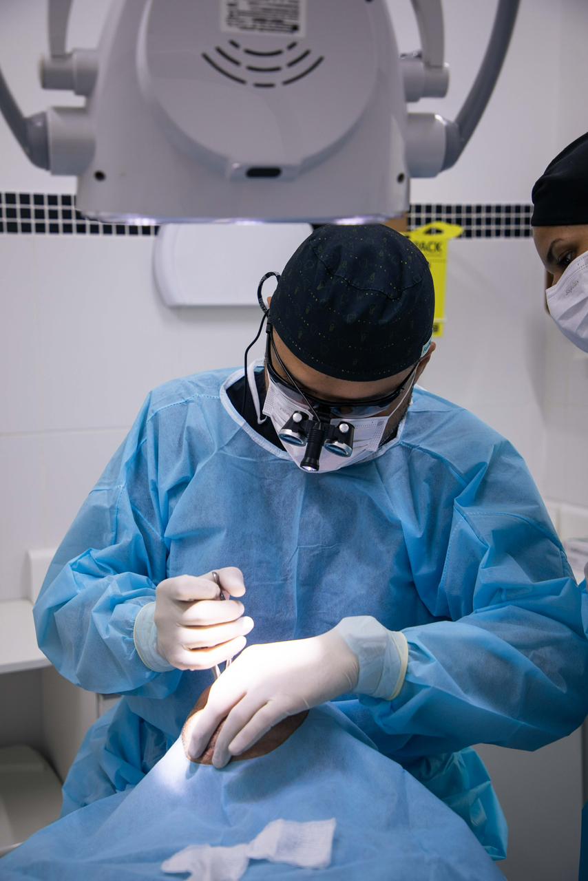 Cirurgia odontológica em andamento com auxiliar — protocolo de biossegurança e equipamento radiográfico.