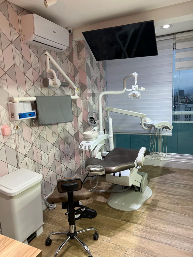 Consultório 1 com cadeira odontológica, equipo, raio-x acoplado e ambientação em tons rosa e mármore.