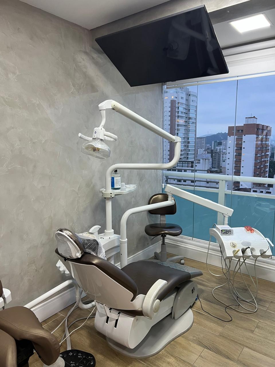 Consultório 2 com cadeira odontológica e vista panorâmica de Santos pela janela.